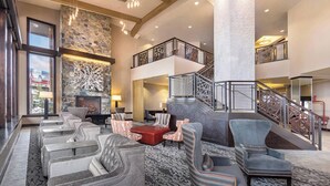 A spacious lobby with a stone fireplace, multiple seating areas, and a staircase connecting two floors.