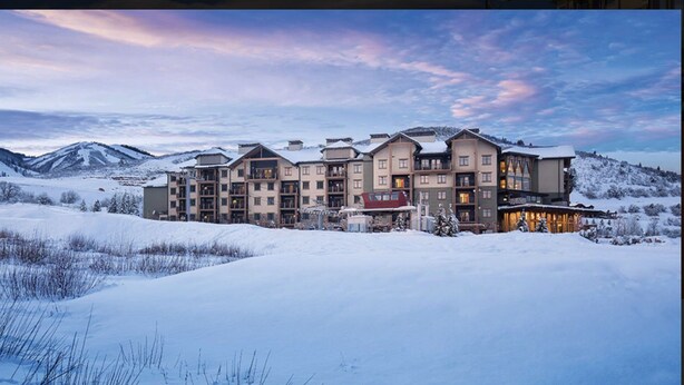 A multi-story hotel with a snow-covered landscape and mountains in the background.
