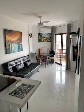 Una sala de estar moderna con un sofá de cuero negro, una mesa de comedor con sillas y un ventilador de techo.