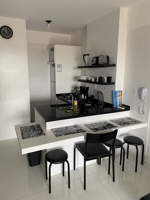 Una cocina moderna con una isla central, sillas negras, un refrigerador y un reloj en la pared.