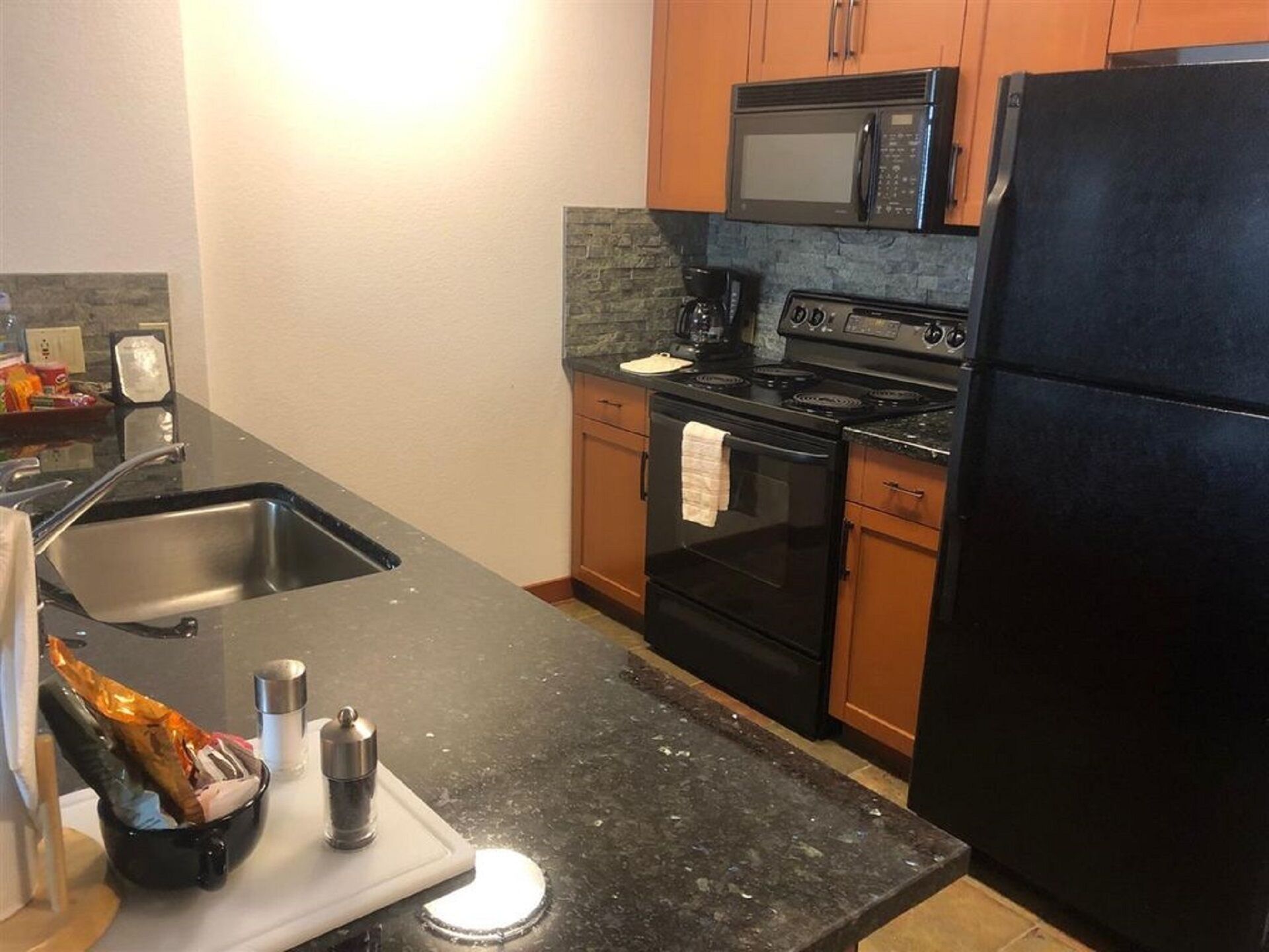 A kitchen with a black countertop, stainless steel sink, black stove, and a black refrigerator.