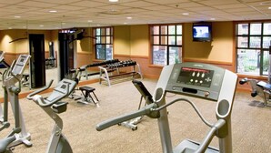 Un gimnasio con cintas de correr, una máquina de remo y una pantalla de televisión.