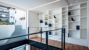 Un interior moderno con barandilla de cristal, estanterías blancas y vistas a un balcón exterior.
