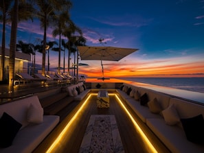 Vista del atardecer desde una terraza con sillones y una mesa, con vista al océano.