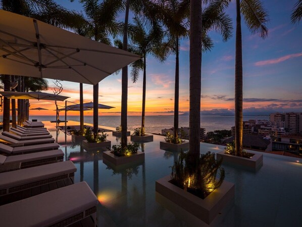 An infinity pool with palm trees and lounge chairs, overlooking a sunset view.