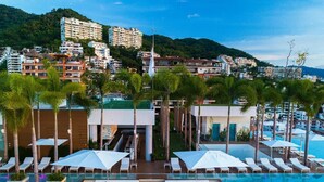 A resort pool area with sun loungers, umbrellas, and a view of the surrounding buildings.