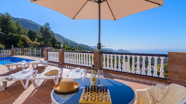 A poolside area with lounge chairs, a table with a chess set, and a bottle of wine. - Villa el Pedregal Frigiliana by Ruralidays (Málaga)