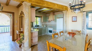 A spacious kitchen with a dining area, featuring a large granite table, wooden chairs, and a chandelier. - Villa el Pedregal Frigiliana by Ruralidays (Málaga)