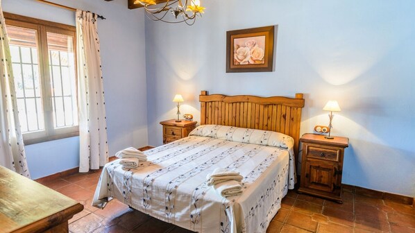 A bedroom with a wooden bed, two bedside tables with lamps, a window with curtains, and a framed picture on the wall. - Mansion Piedras Blancas Colmenar by Ruralidays (Málaga)