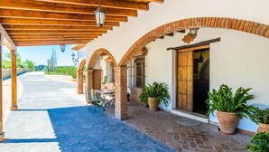 A covered outdoor area with brick arches, a table with chairs, and potted plants. - Mansion Piedras Blancas Colmenar by Ruralidays (Málaga)