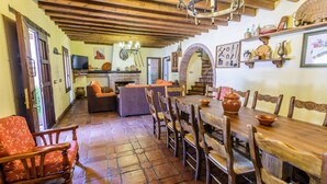 A rustic interior with a wooden dining table, chairs, a fireplace, and a staircase leading to an upper level. - Mansion Piedras Blancas Colmenar by Ruralidays (Málaga)