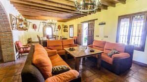 A cozy living room with orange sofas, a wooden table, and a chandelier. - Mansion Piedras Blancas Colmenar by Ruralidays (Málaga)