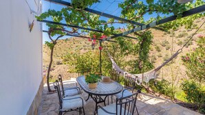 An outdoor patio with a table and chairs, a hammock, and a pergola with vines. - Casa Jazmín Azul Cómpeta by Ruralidays (Málaga)