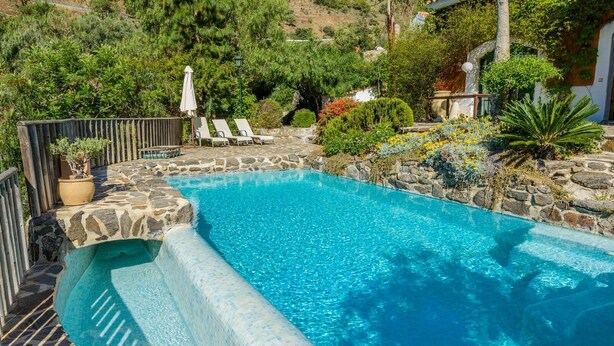A swimming pool with stone edges, surrounded by lounge chairs and potted plants. - Hidalgo de Arenas by Ruralidays (Málaga)