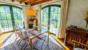 A dining area with a glass table and chairs, a wooden cabinet, and a view of greenery through large windows. - Hidalgo de Arenas by Ruralidays (Málaga)