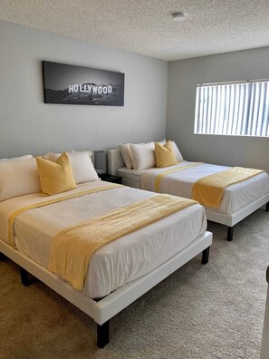 A hotel room with two beds, a large window with blinds, a ceiling light, and a wall-mounted sign that reads "HOLLYWOOD". - Hollywood Spacious Place (Los Angeles)