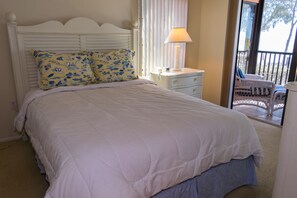 Une chambre à coucher avec un lit, deux oreillers, une table de chevet, une lampe et une vue sur le balcon extérieur.