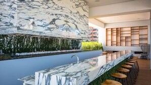 A modern bar area with a marble countertop, wooden stools, and a green vertical garden. - PIER 57 - 208 | 2BR Condo with Best Rooftop View (Puerto Vallarta)