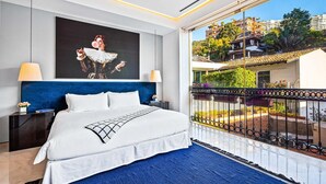 A hotel room with a large bed, a balcony with a view of buildings and greenery, and a painting on the wall. - PIER 57 - 208 | 2BR Condo with Best Rooftop View (Puerto Vallarta)