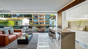 A modern living room with a glass coffee table, a leather sofa, and a view of a residential area. - PIER 57 - 208 | 2BR Condo with Best Rooftop View (Puerto Vallarta)