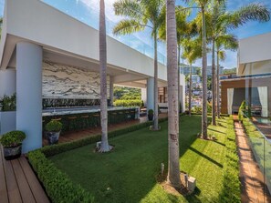 A modern outdoor area with a wooden deck, a grassy lawn, and tall palm trees. - PIER 57 - 208 | 2BR Condo with Best Rooftop View (Puerto Vallarta)
