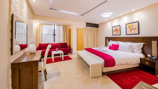 Una habitación de hotel con cama, escritorio, sofá rojo y alfombra roja.