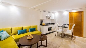 Un espacio habitable compacto con un sofá amarillo, una pequeña mesa de comedor y una kitchenette.
