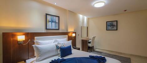 Una habitación de hotel con una cama grande, mesitas de noche, un escritorio y dos lámparas fijadas a la pared.