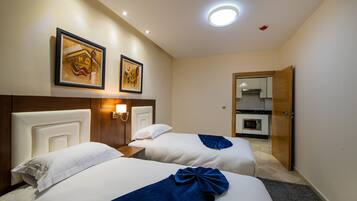 Une chambre d’hôtel avec deux lits, une tête de lit en bois, une lampe fixée au mur et une porte donnant sur une petite cuisine.
