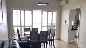 Een woonkamer met een zwarte leren bank, gestreept fauteuils, een gele bijzettafeltje en een groot raam met uitzicht.