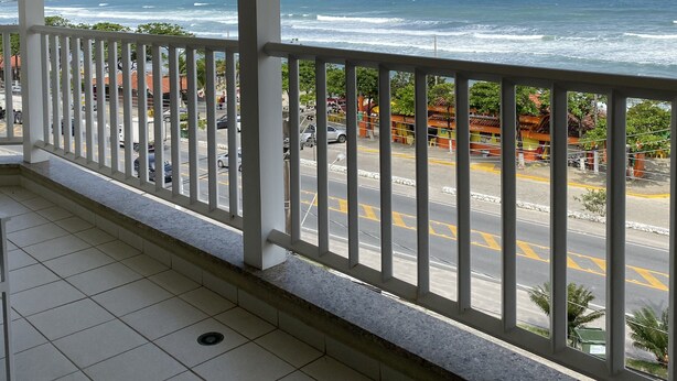 Een overdekt balkon met uitzicht op de oceaan en een drukke straat.