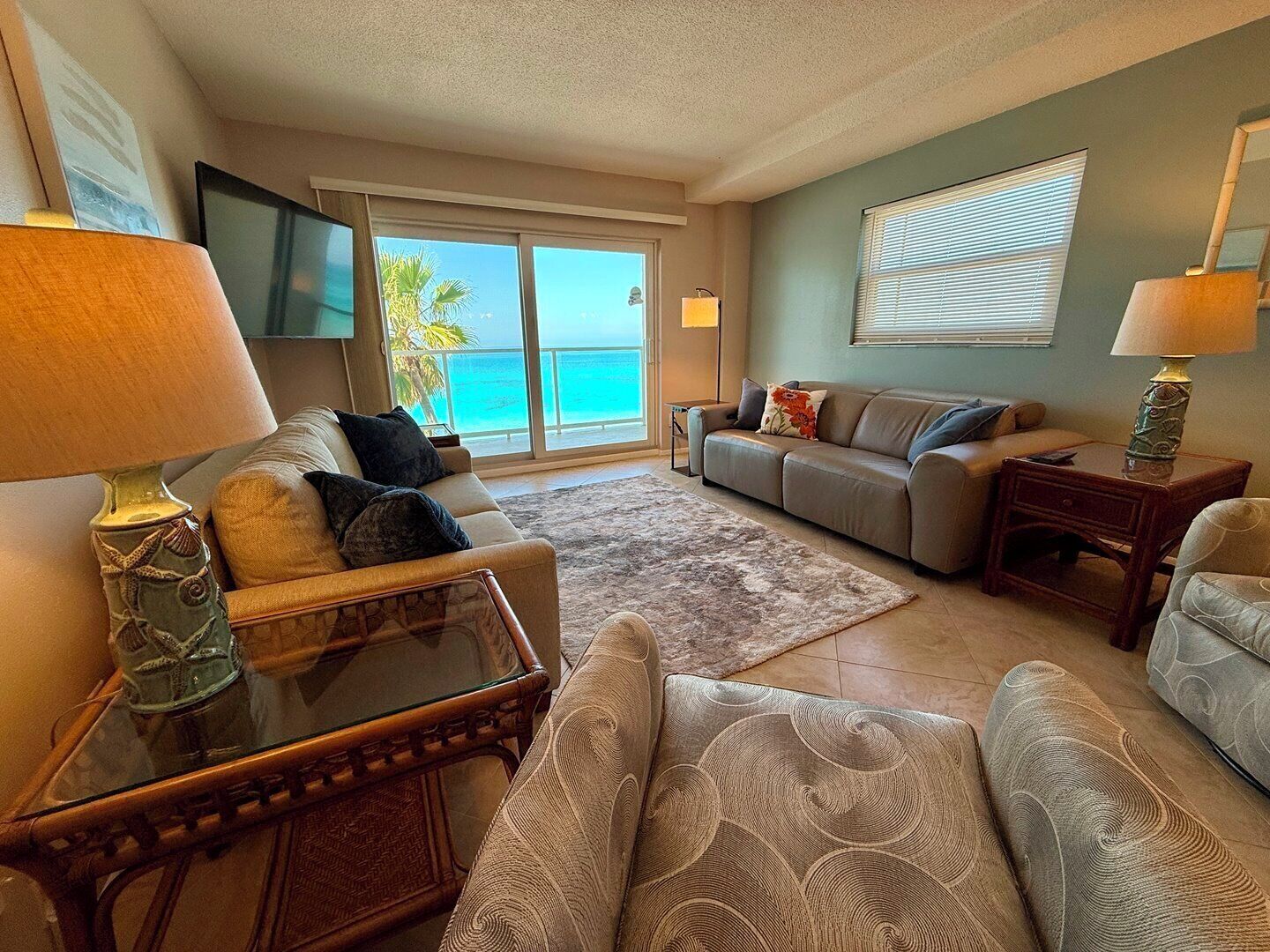A living room with a sofa, a coffee table, a TV, and a view of the ocean.