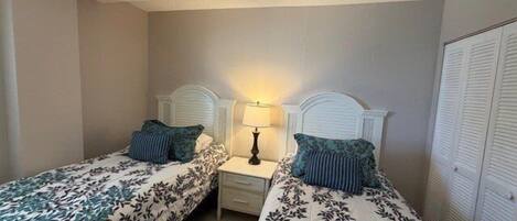 Habitación de hotel con dos camas individuales, una mesita de noche con lámpara, un armario y una pared lisa.