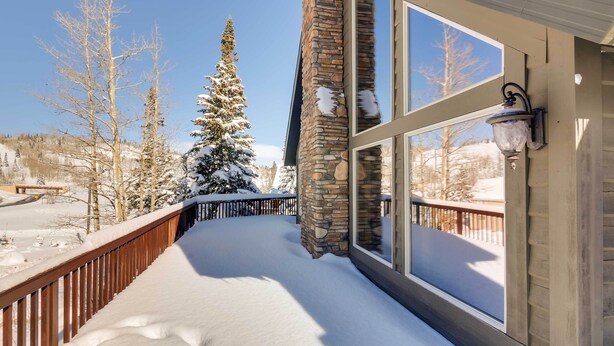 A snow-covered deck with a stone pillar and a window with a wall-mounted light fixture. - Group Ski Getaway Near the Base of Chairlift 8! (Brian Head)