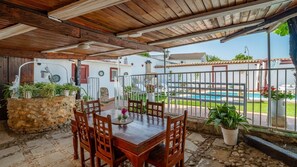 Une terrasse couverte avec une table et des chaises en bois, entourée de murs en pierre et de plantes en pot.
