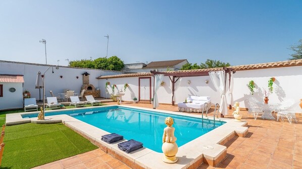Une piscine avec des chaises longues, une pergola et une statue.