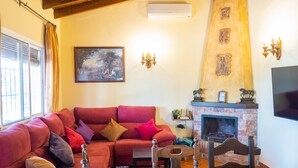 A cozy living room with a red sofa, a fireplace, a painting, and a television. - Cubo's Finca Los Dragos. Pool, wifi and AC/heating (Alhaurín el Grande)