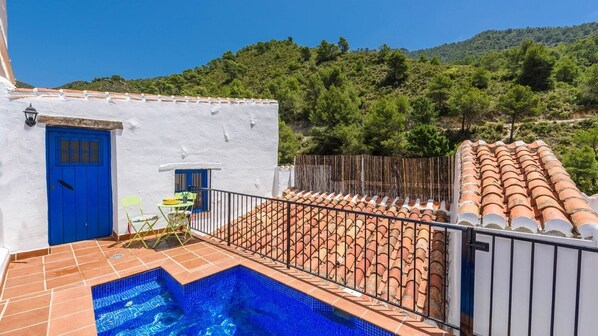 A white building with a blue door, a small outdoor seating area, and a swimming pool. - Casita Las Mariposas Frigiliana by Ruralidays (Málaga)