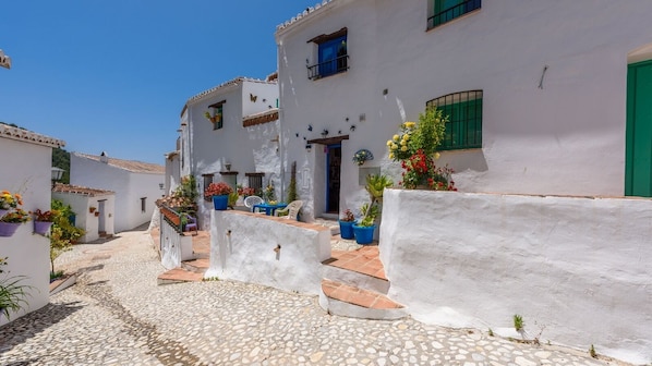 A narrow cobblestone street with white buildings, a staircase, and potted plants.