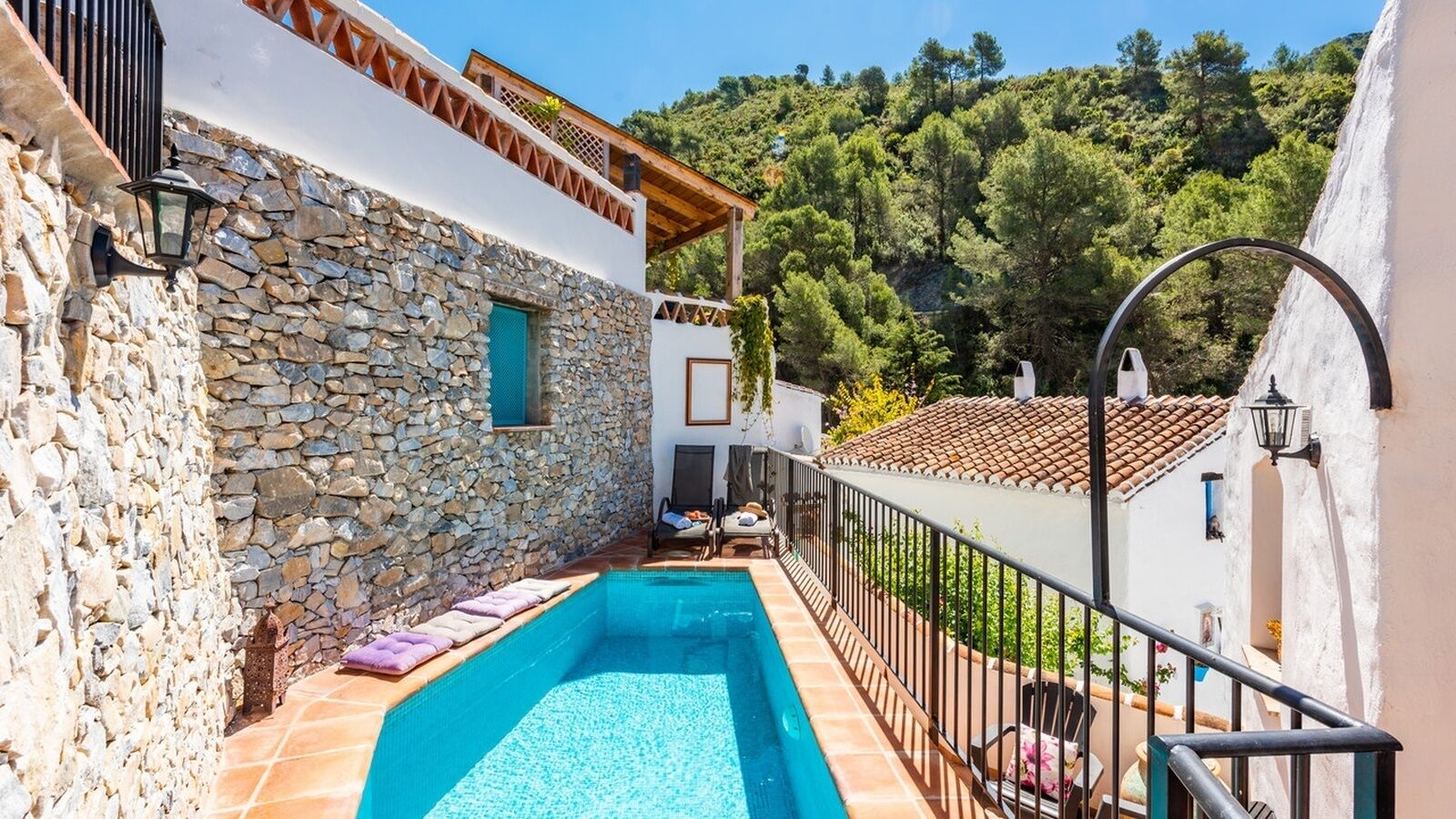 Edificio de paredes de piedra con piscina, zona de estar al aire libre y vistas a una ladera boscosa.