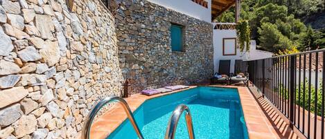 A stone-walled pool with a metal ladder, surrounded by a tiled deck and a metal fence.