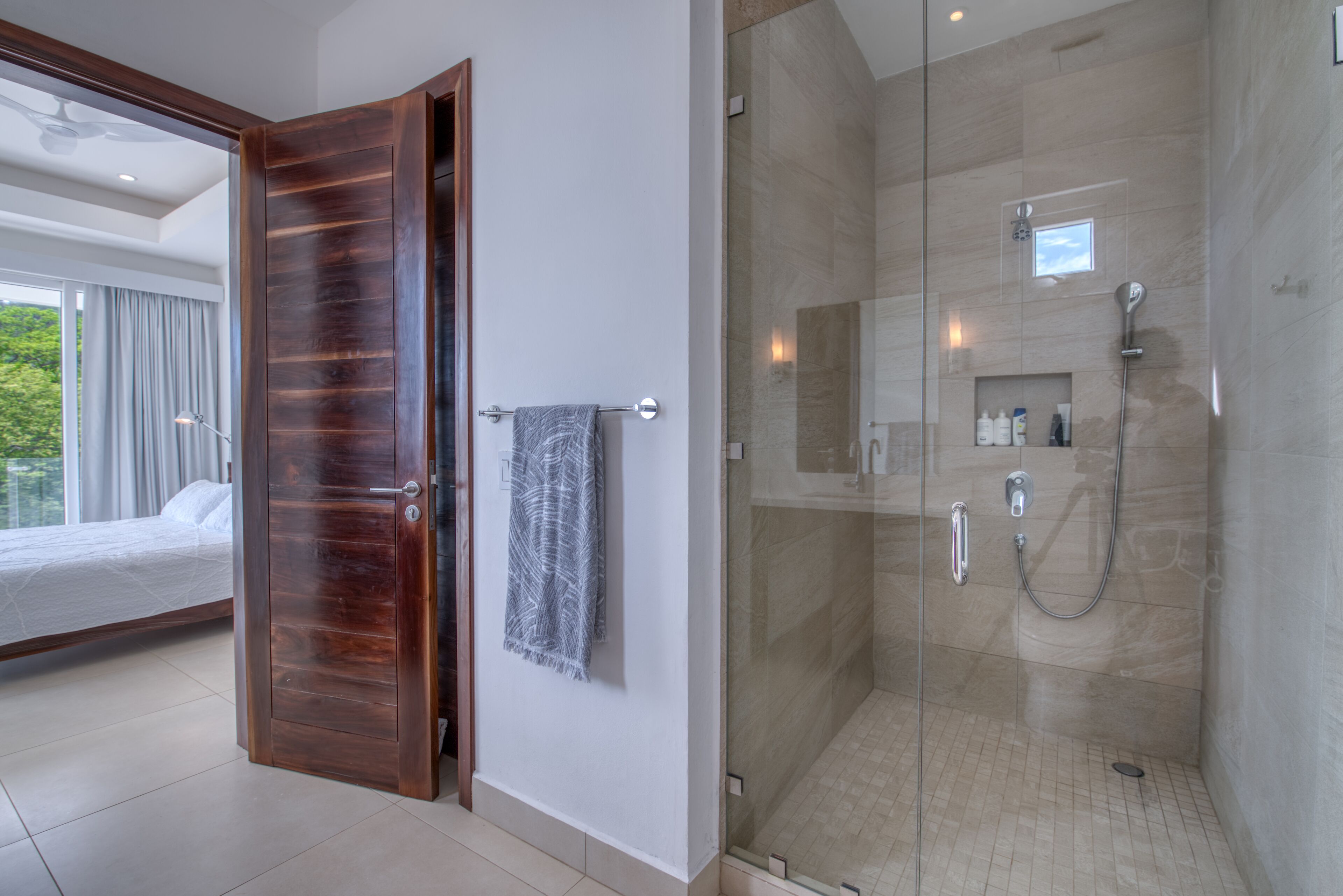 Ein modernes Badezimmer mit einer einachig verglasten Dusche, einer Holztür und einem sichtbaren Handtuchhalter.