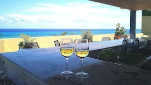 A balcony with two glasses of white wine, a potted plant, and a view of the ocean. - Singular Joy Vacation Rentals (Playa del Carmen)