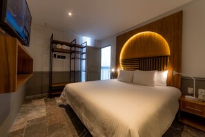 A modern hotel room with a large bed, wooden headboard, and a TV mounted on the wall. - Singular Joy Vacation Rentals (Playa del Carmen)