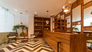 A reception area with a wooden reception desk, seating with chairs, a herringbone patterned floor, and wooden shelving with plants. - Singular Joy Vacation Rentals (Playa del Carmen)