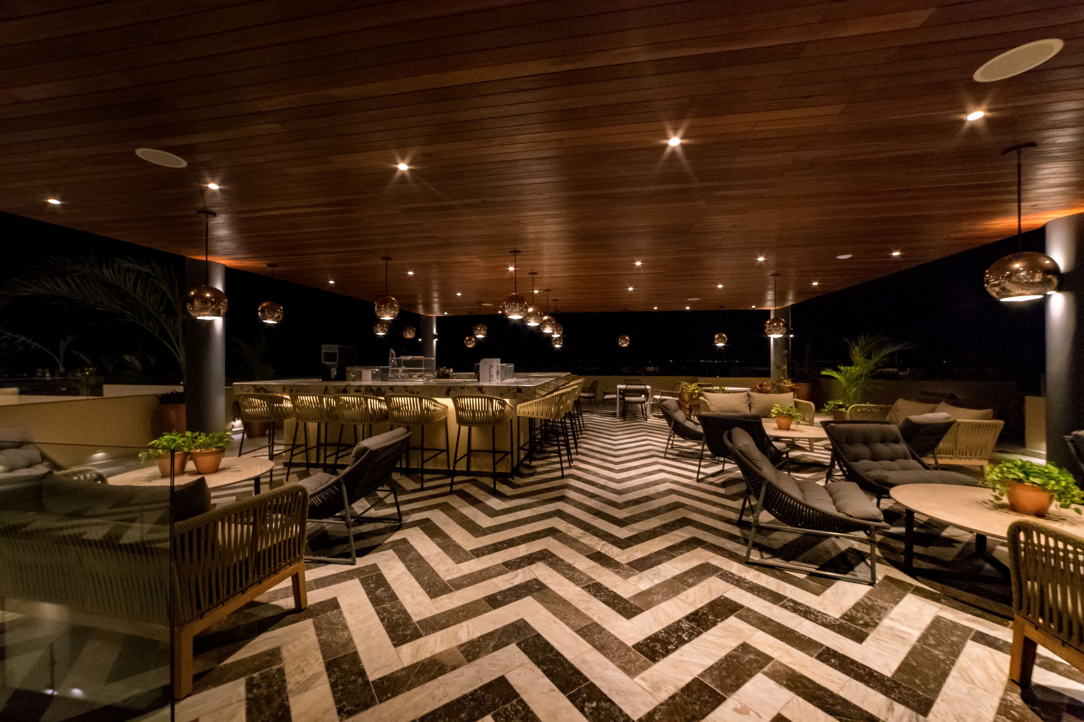 An outdoor bar area with a chevron-patterned floor, wooden ceiling, and modern lighting fixtures.