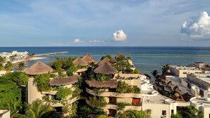 A coastal resort with thatched-roof buildings, palm trees, and a view of the sea and pier. - Singular Joy Vacation Rentals (Playa del Carmen)