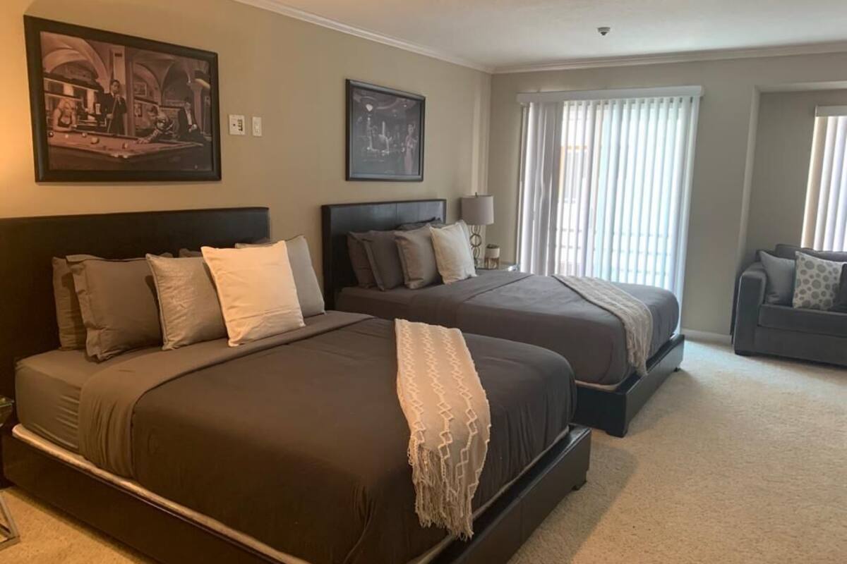 A hotel room with two beds, a sofa, and a large window with curtains.