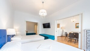 Habitación de hotel con dos camas, televisor, candelabro y zona de comedor con sillas y una mesa.