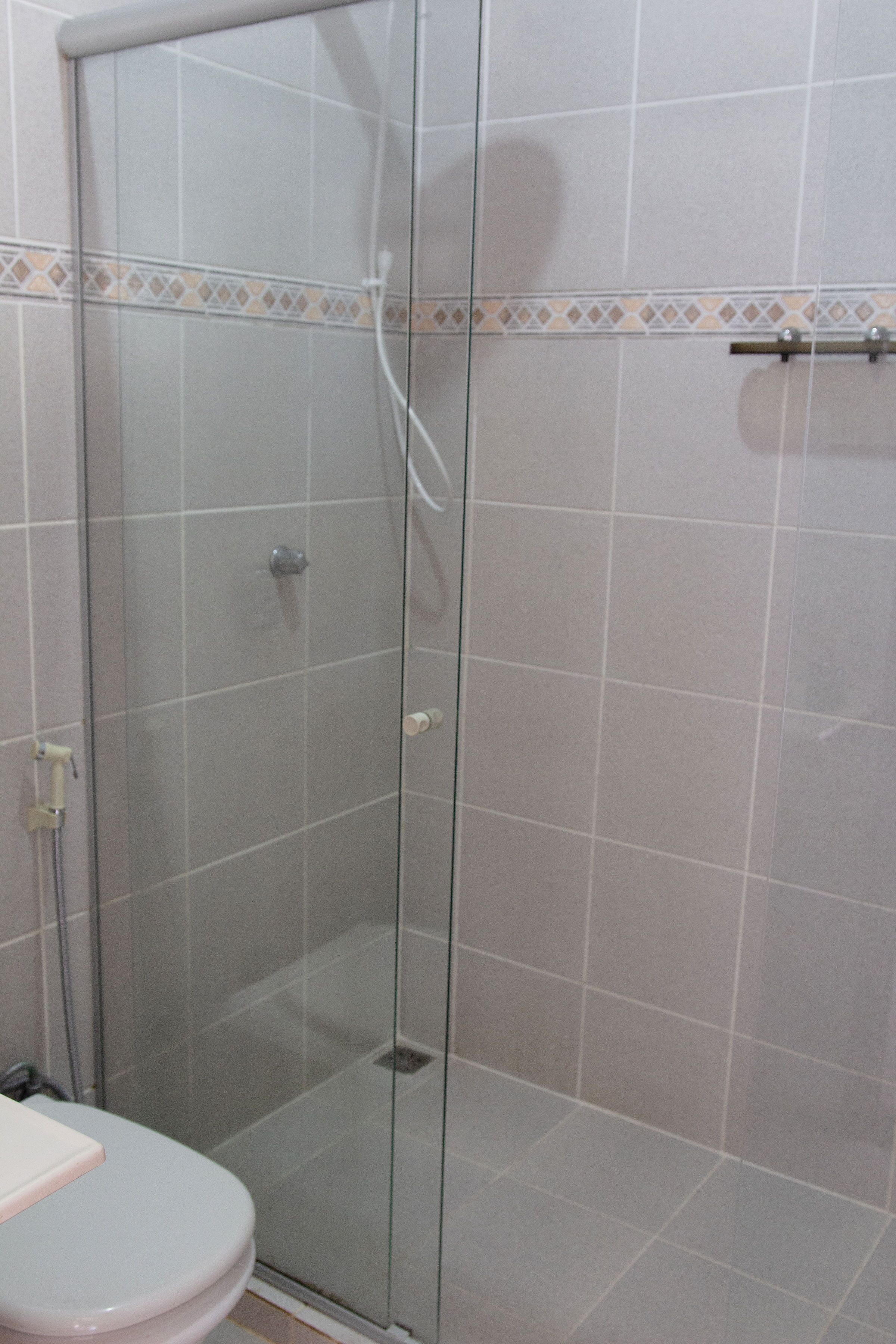 Une cabine de douche fermée par des parois en verre, avec un mur carrelé, des toilettes et un pommeau de douche.